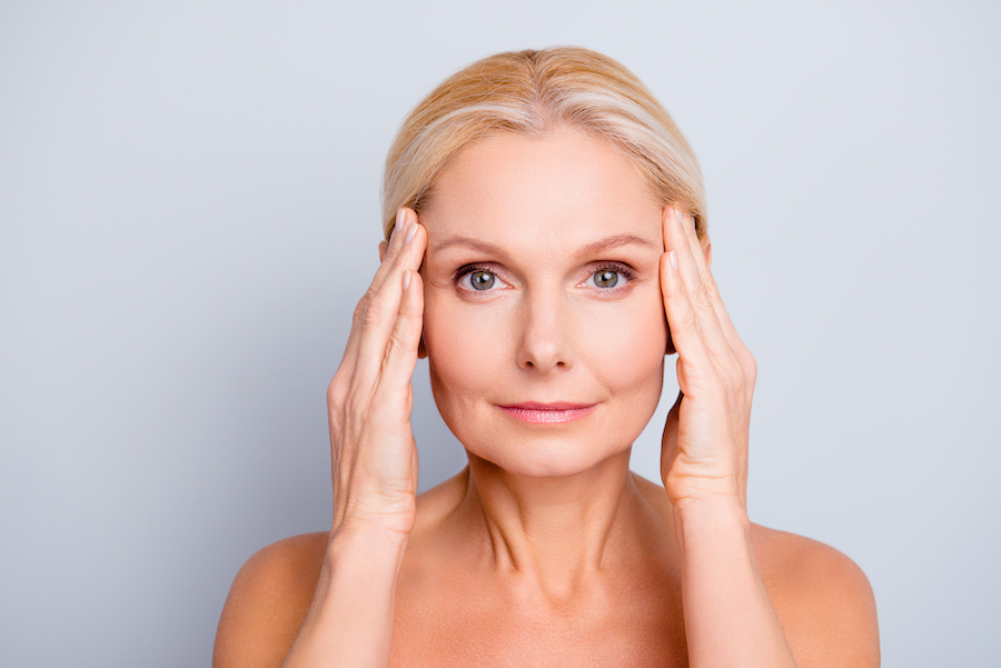 Mature woman touches her temples after BOTOX treatment to smooth out her wrinkles