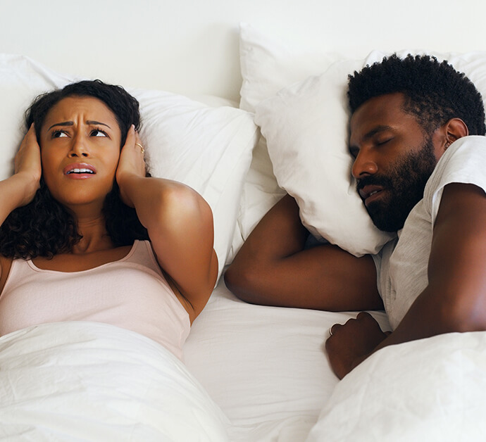 woman covering her ears with her pillow as her husband snores
