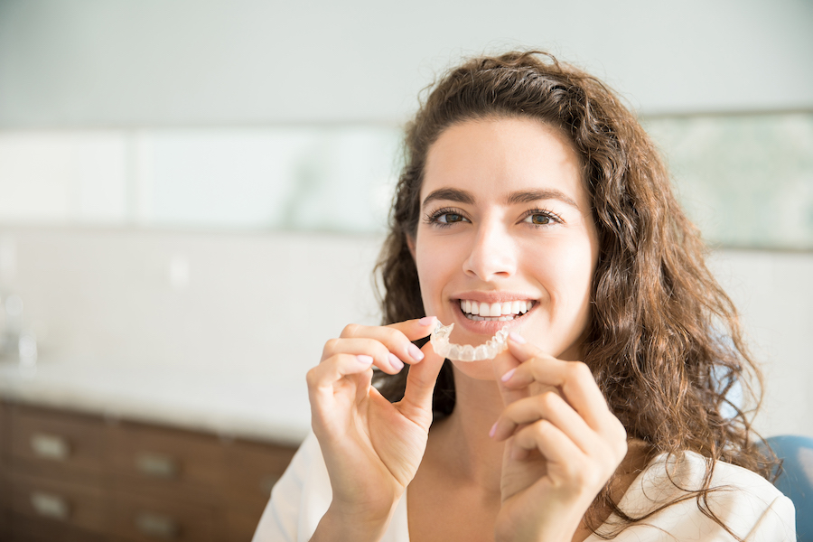 photograph of young woman holding invisalign clear aligners, can I use invisalign with dental crowns